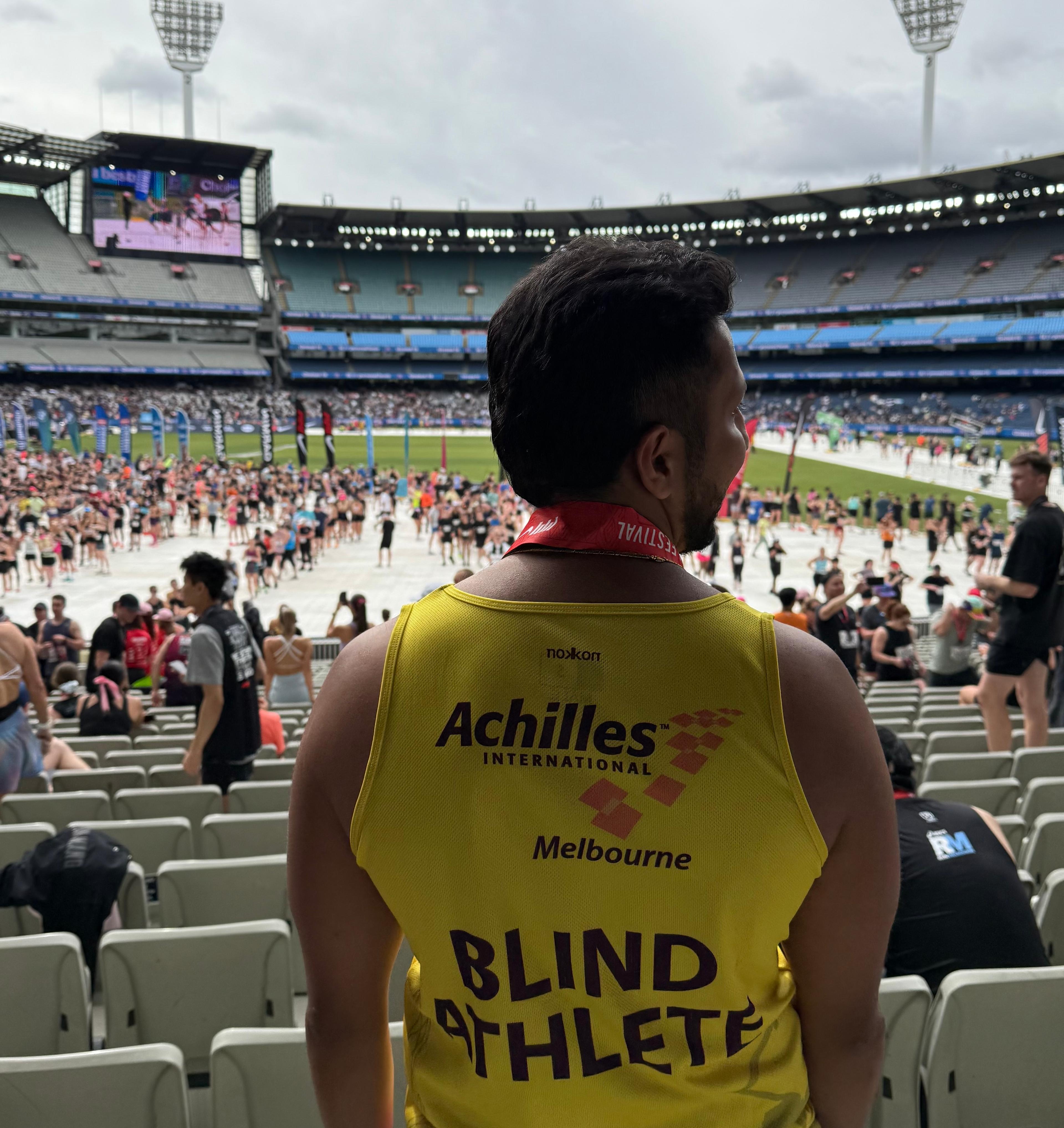 Aadi standing in the MCG with his back to the camera. The back of his singlet has the words Blind Athlete printed on it